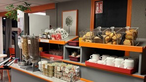 Mostrador de cafetería con diversas opciones de comida, una máquina de café y una planta.