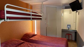 Een studentenkamer met een stapelbed, een bureau met een computerscherm en een klein krukje.