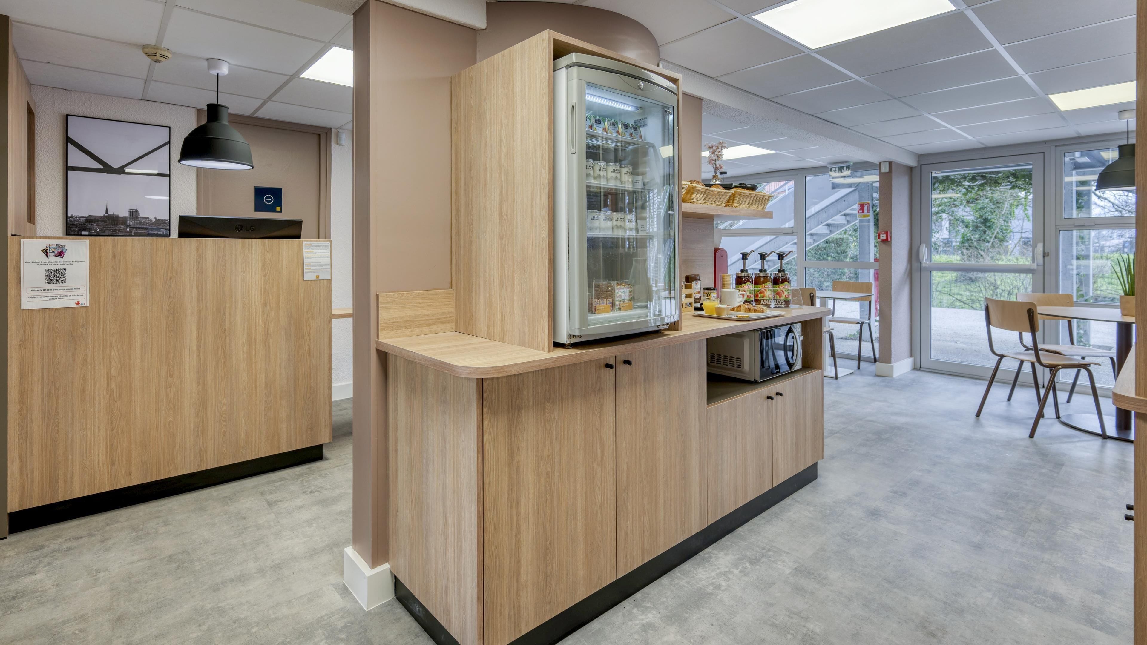 Un caffè moderno con arredi in legno, una vetrina che espone bevande e una vista attraverso ampie finestre.