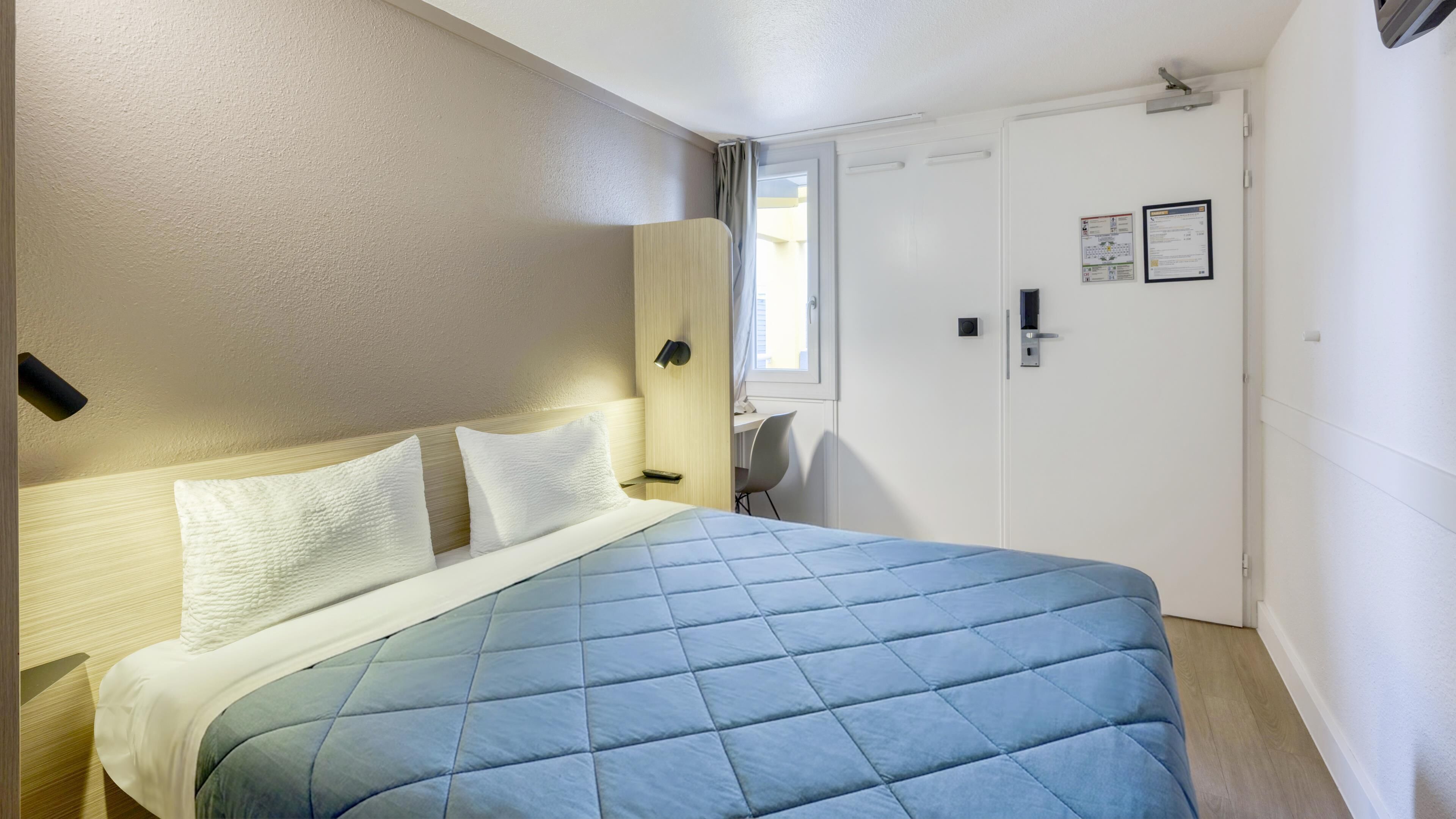 A bedroom with a bed, a desk, and a door.