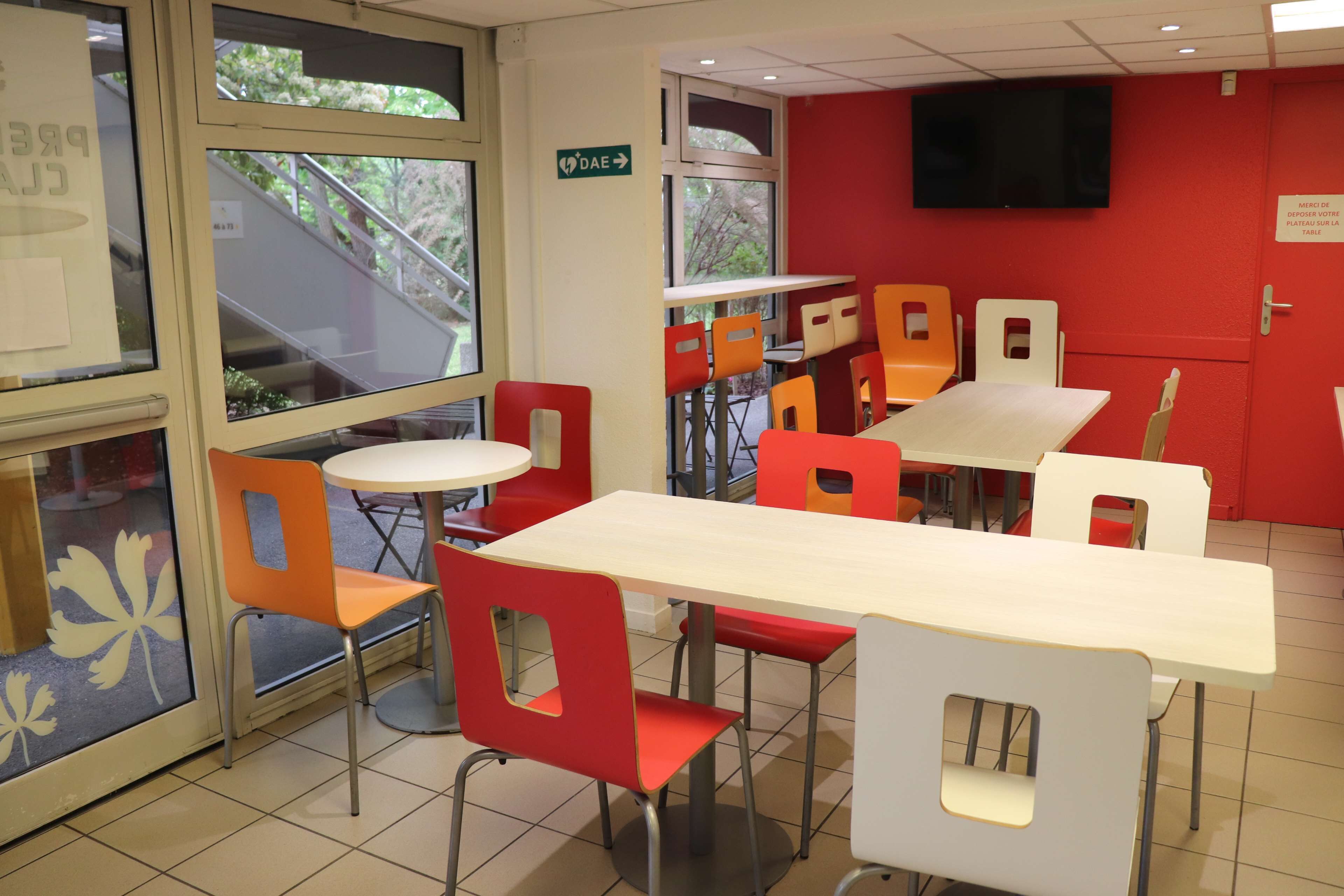 Un comedor con sillas rojas y blancas, una mesa larga y un televisor en la pared.