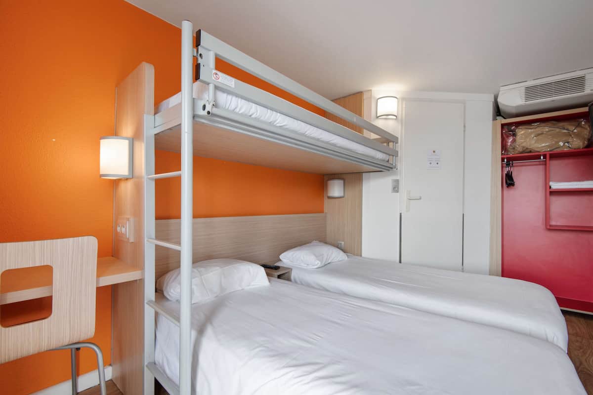 Quarto de hotel com beliche, uma mesa e um guarda-roupa.