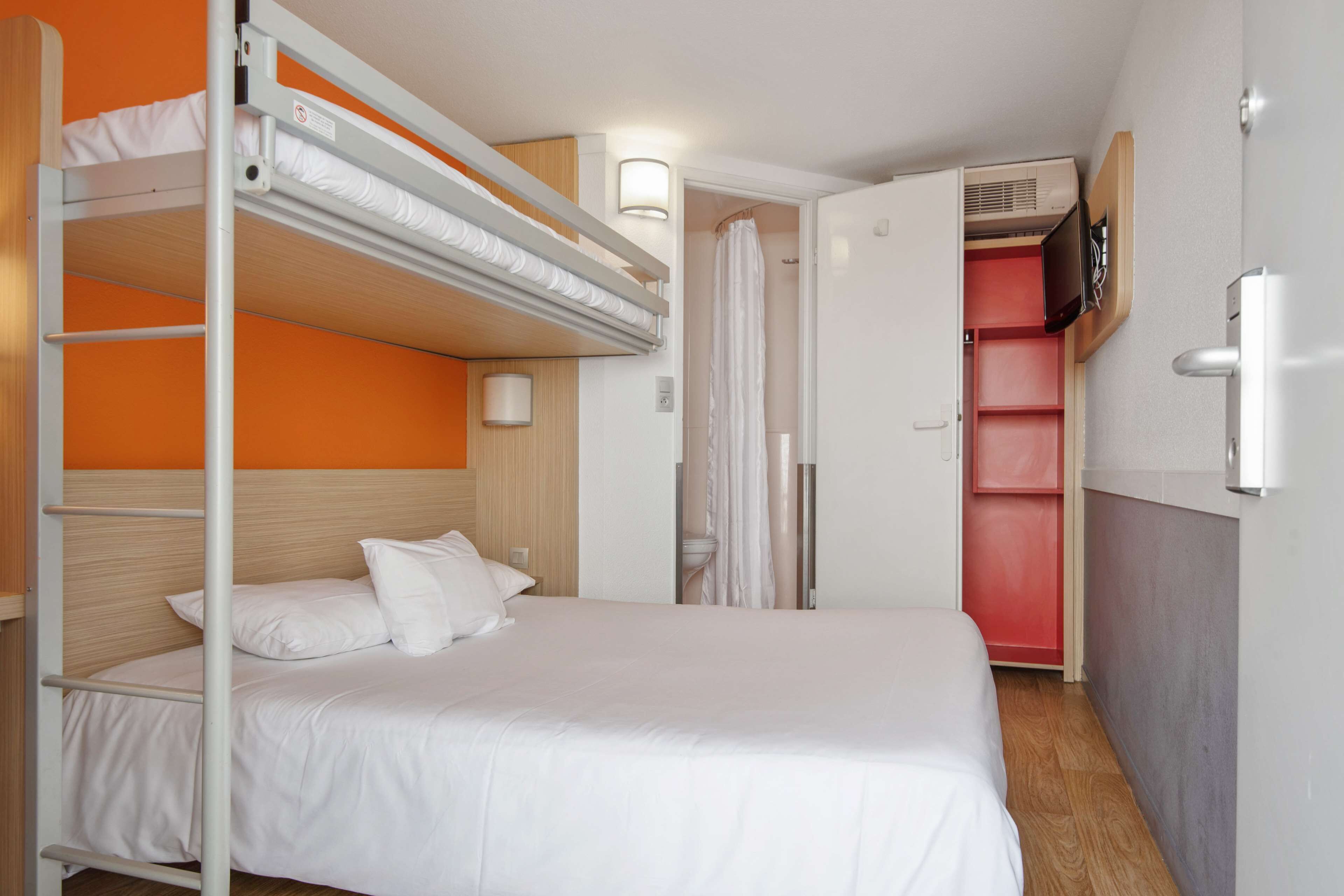 Una cama litera con ropa de cama blanca, cabecera de madera y pared blanca.