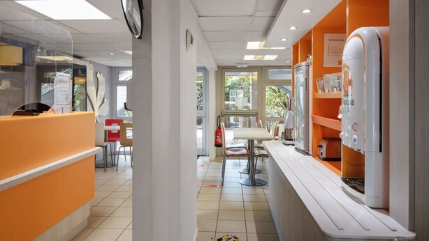 Interior moderno de restaurante con mostrador, zona de estar y un reloj a la vista.