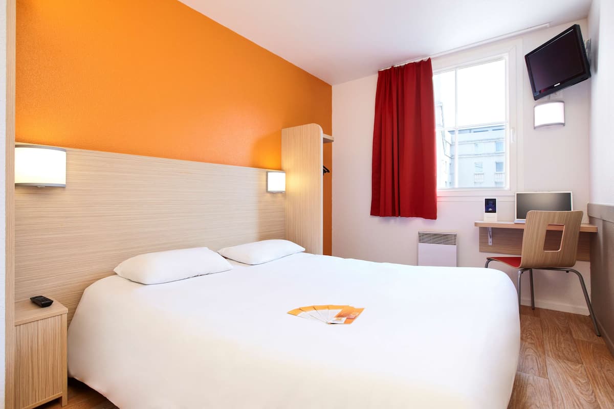 Ein Hotelzimmer mit Bett, Schreibtisch, Stuhl, Fernseher und einem Fenster mit Vorhängen.