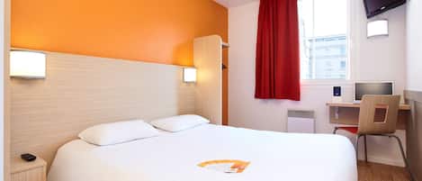 A hotel room with a bed, a desk, a chair, a TV, and a window with curtains.