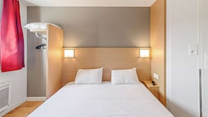 Une chambre d’hôtel avec un lit, deux lampes de chevet, une table de nuit, un rideau rouge et un radiateur fixé au mur.
