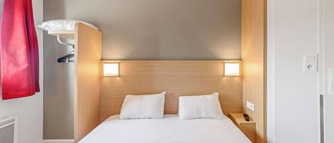A hotel room with a bed, two bedside lamps, a nightstand, a red curtain, and a wall-mounted heater.