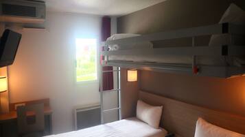Une chambre d’hôtel avec des lits superposés, un bureau, une chaise, une télévision et une fenêtre avec des rideaux.