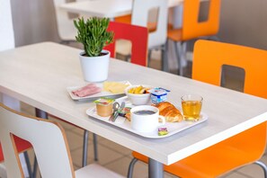 Bandeja de desayuno con café, croissant, fruta, yogur y una planta sobre una mesa.
