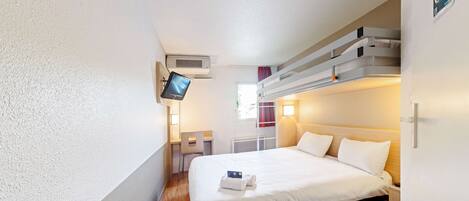 A hotel room with a bed, a desk, a chair, a TV, and a staircase.