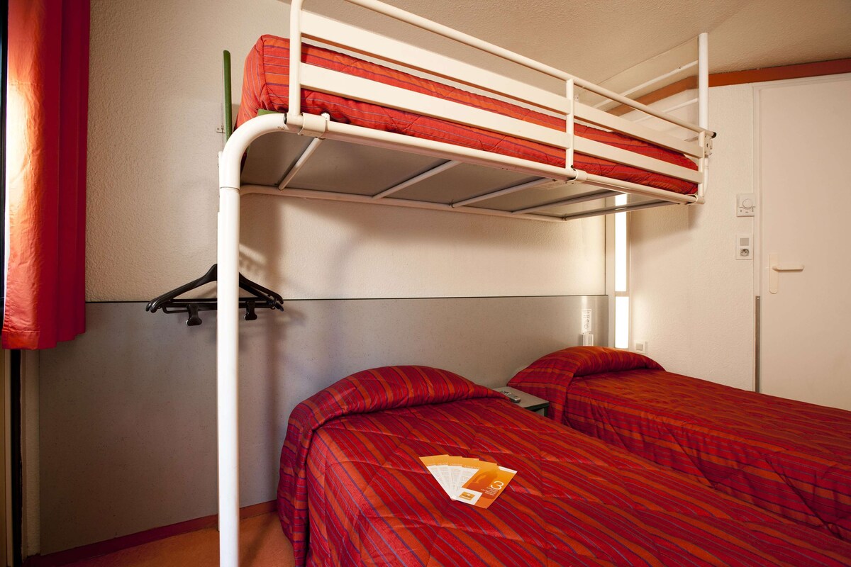 Habitación con literas, una colcha roja a rayas, una pared blanca y una puerta.