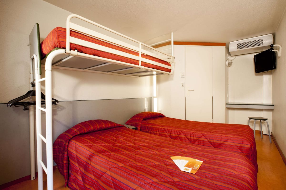 Ein Schlafzimmer mit Etagenbett, einer roten Bettdecke, einer weißen Klimaanlage und einem kleinen Hocker.