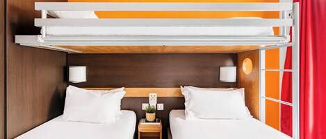 Habitación con literas, dos camas, una mesita de noche con lámpara y una ventana con cortinas anaranjadas.