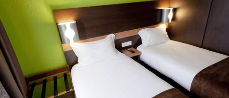 Habitación de hotel con dos camas, cabecero de madera, mesita de noche y control remoto, y pared verde.
