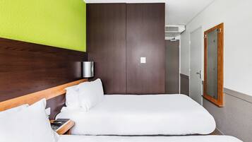 A hotel room with a bed, a bedside table with a lamp, a mirror, and a door to a bathroom.
