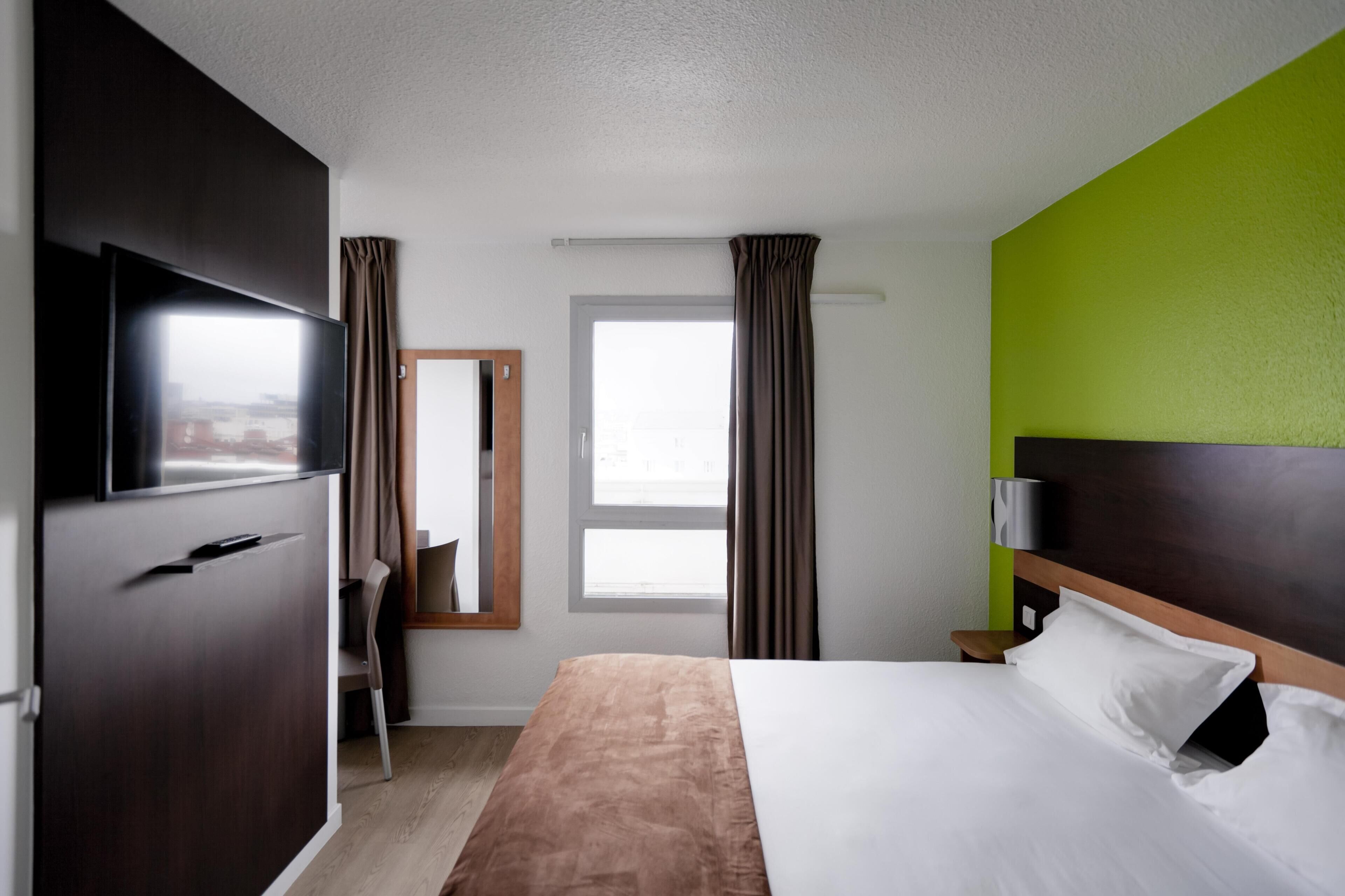 Habitación de hotel con cama, televisión, espejo, ventana y cortinas.