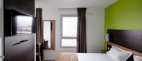 Habitación de hotel con cama, televisión, espejo, ventana y cortinas.
