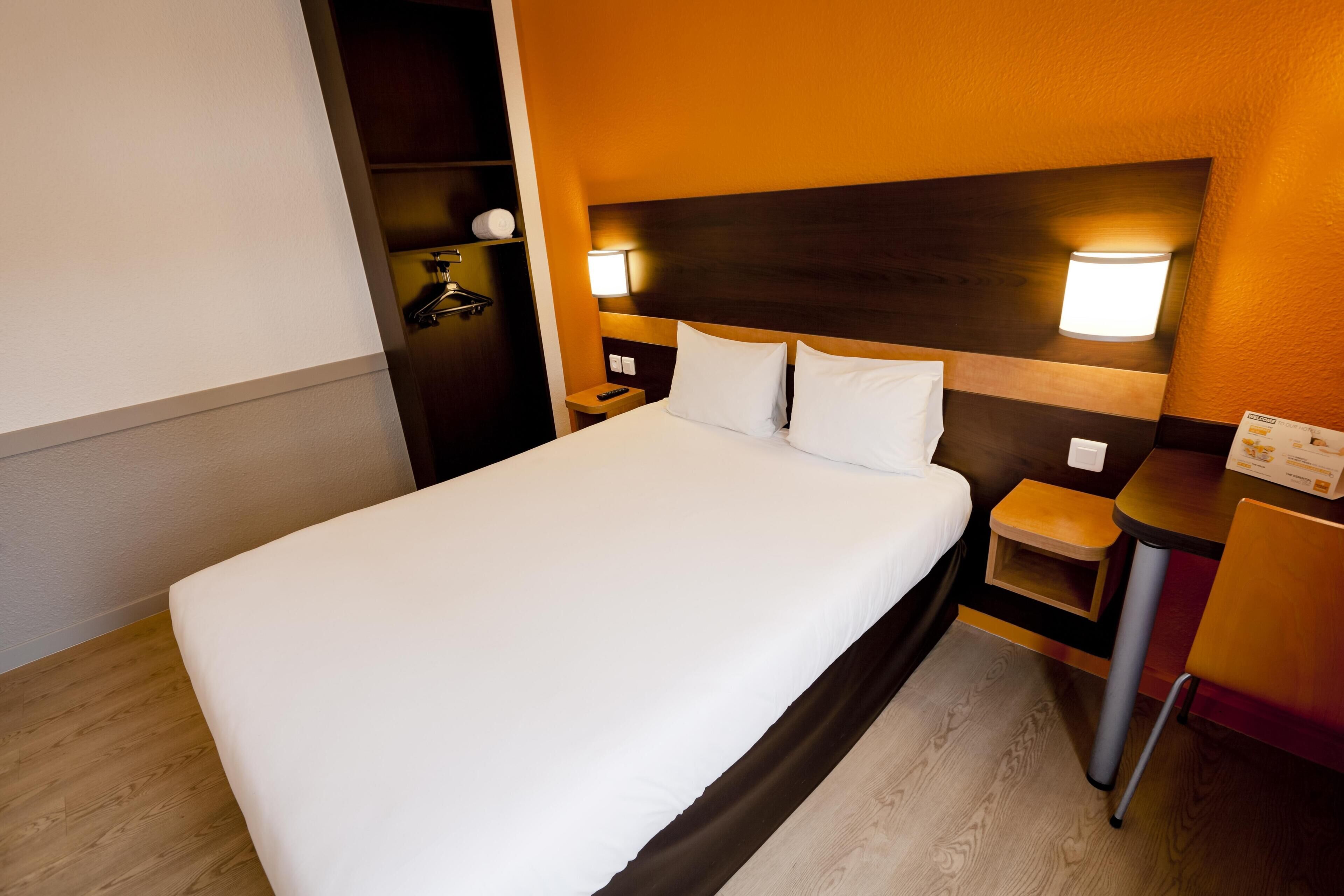 A hotel room with a large bed, bedside tables, a nightstand, and a wall-mounted lamp.