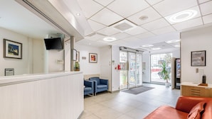 A reception area with a counter, blue chairs, a red sofa, and a glass door leading outside. - Premiere Classe Lyon Centre - Gare Part Dieu (Lyon)