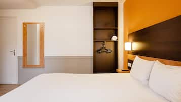 Habitación de hotel con cama, espejo, armario y mesita de noche con lámpara.