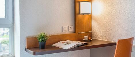 A modern room with a wooden desk, a potted plant, a magazine, a cup, and a television mounted on the wall.