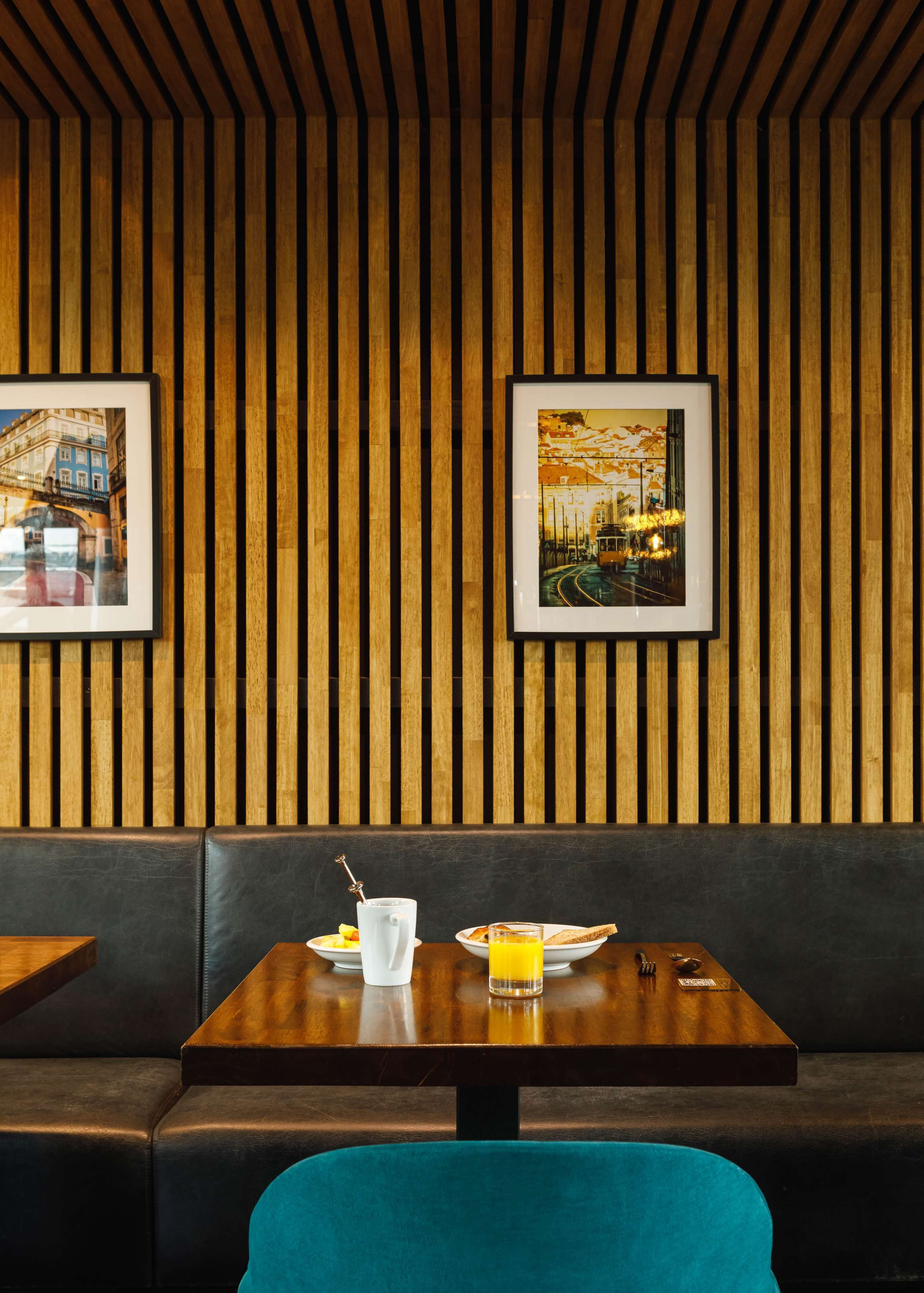 A restaurant with wooden panel walls, framed pictures, a wooden table, a blue chair, and a black leather booth.