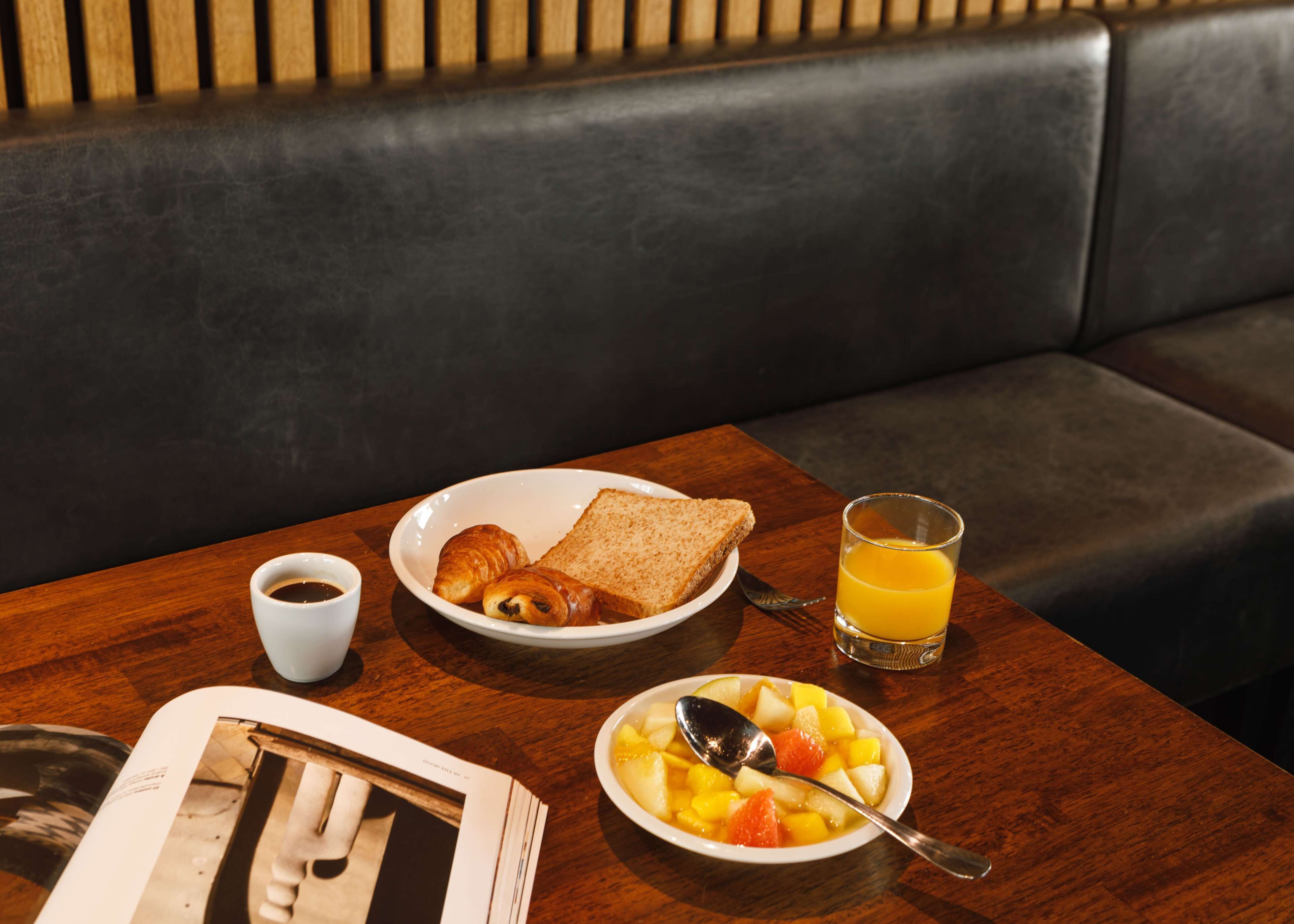 A breakfast setting with croissants, toast, orange juice, and a fruit bowl on a wooden table.