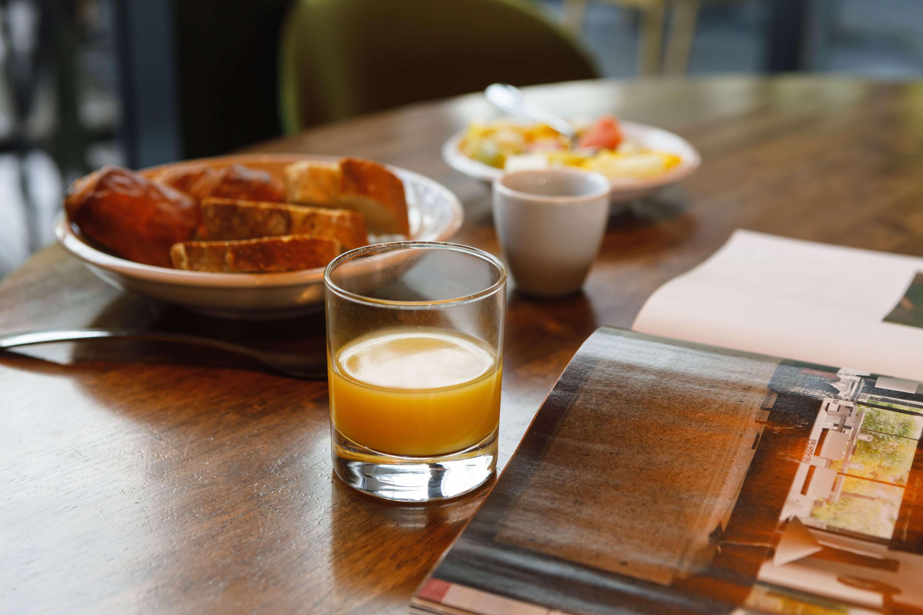 Desayuno con tostadas, un vaso de zumo de naranja y un plato de huevos y verduras sobre una mesa de madera.