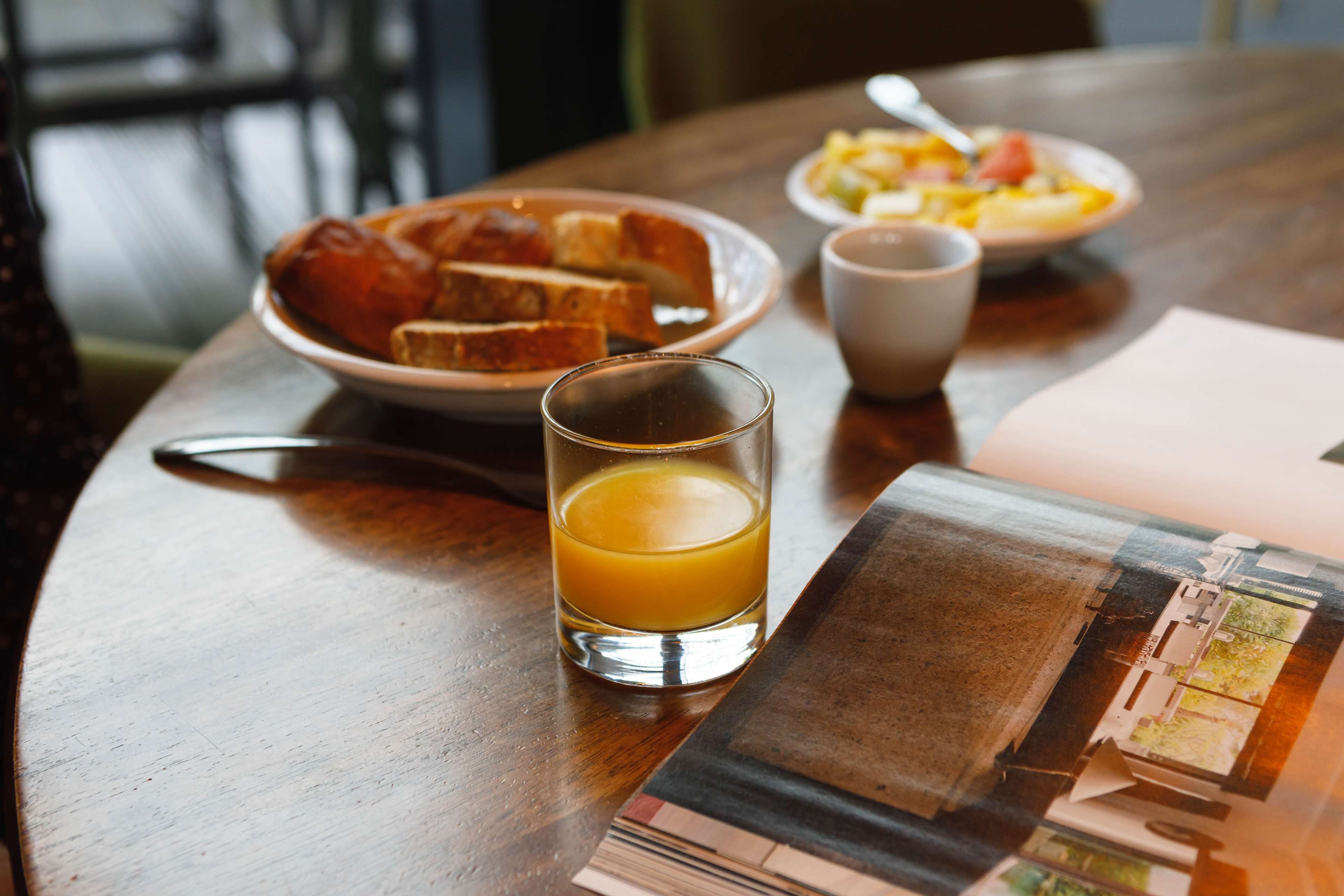 Una mesa con un vaso de jugo de naranja, una tostada, un plato de sopa y una taza.