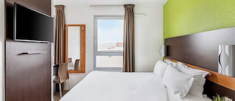 Una habitación de hotel con una cama grande, televisión, escritorio con silla y ventana con cortinas.