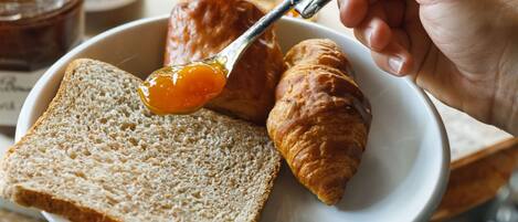 Una persona untando mermelada en un croissant y una rebanada de pan.