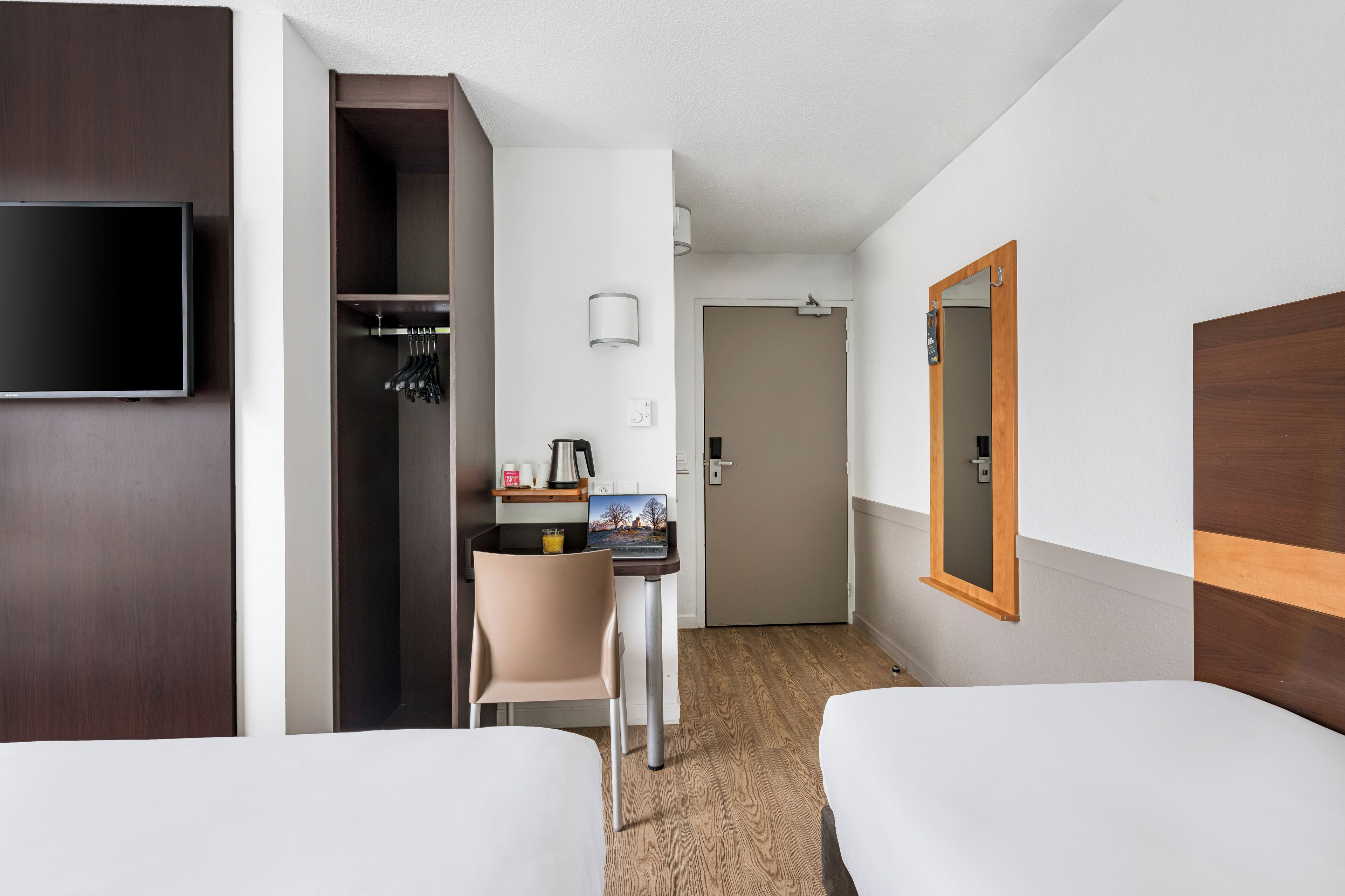 A hotel room with two beds, a desk with a chair, a television, and a wardrobe.