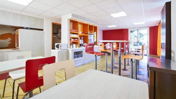 Een modern restaurant met wit en rood decor, meerdere zithoeken en een lichte inrichting.