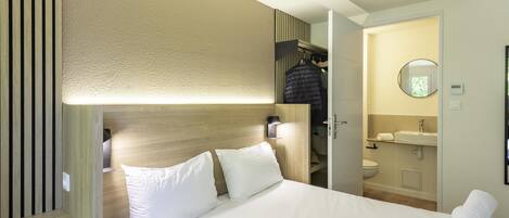 A hotel room with a bed, a bedside table with a remote control, a wardrobe, and a bathroom with a sink and toilet.