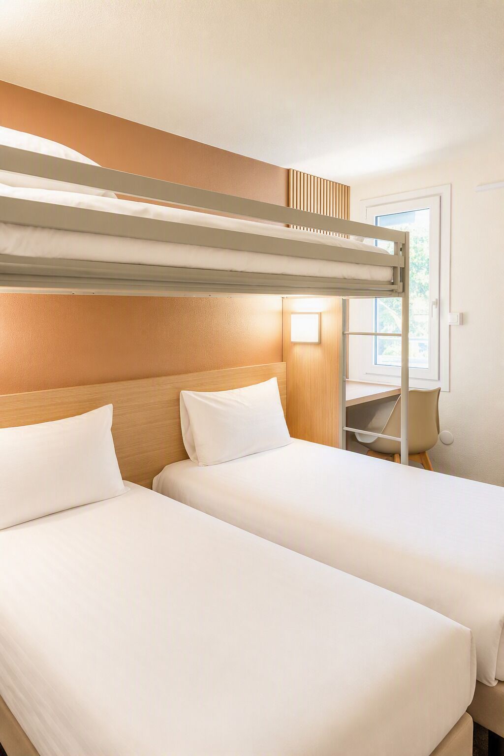Habitación de hotel con dos camas, una litera en la parte superior, un escritorio y una ventana.