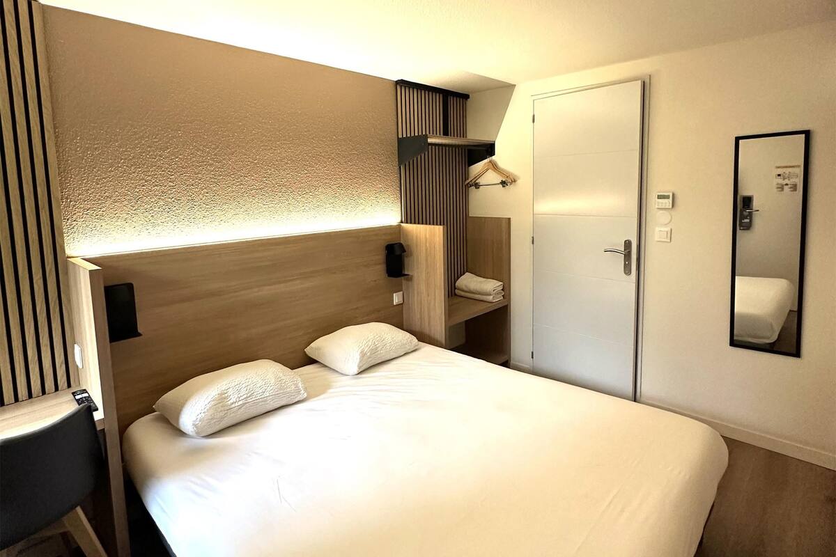 A hotel room with a large bed, a desk, a wardrobe, and a mirror on the wall.