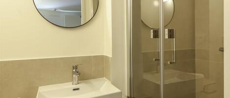 A modern bathroom with a glass-enclosed shower, a white sink, and a round mirror.