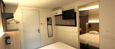 Een moderne hotelkamer met een groot bed, een flatscreen-televisie aan de muur, een ingebouwde airconditioning en een klein zitgedeelte met een houten bank.