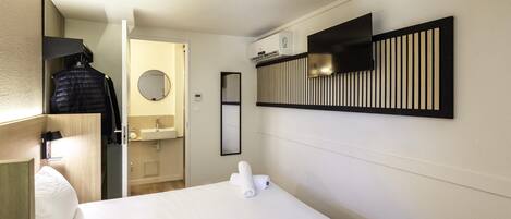 Habitación de hotel con cama, espejo, bata colgada, toalla, armario, lavamanos y aire acondicionado instalado en la pared.