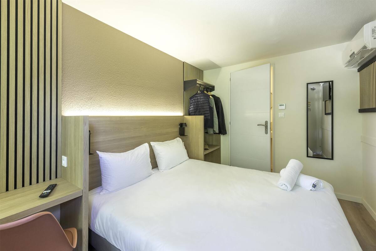 Una habitación de hotel con una cama, un escritorio, una silla, un armario y un espejo.