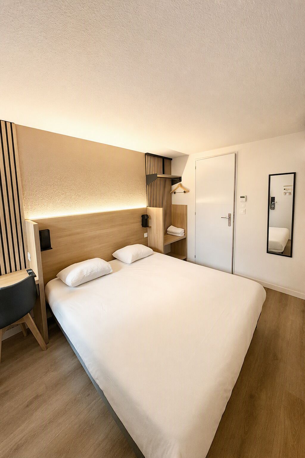 Quarto de hotel com uma cama grande, escrivaninha, guarda-roupa e espelho.