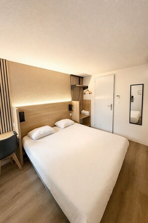 Ein Hotelzimmer mit einem großen Bett, einem Schreibtisch, einem Kleiderschrank und einem Spiegel.