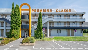 A multi-story hotel with a prominent entrance archway, a sign reading 'PREMIERE CLASSE,' and a parking lot with handicapped parking spaces.