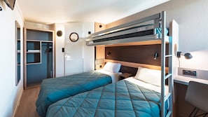 Ein kleines Zimmer mit zwei Etagenbetten, einem kleinen Schreibtisch und einem Kleiderschrank.