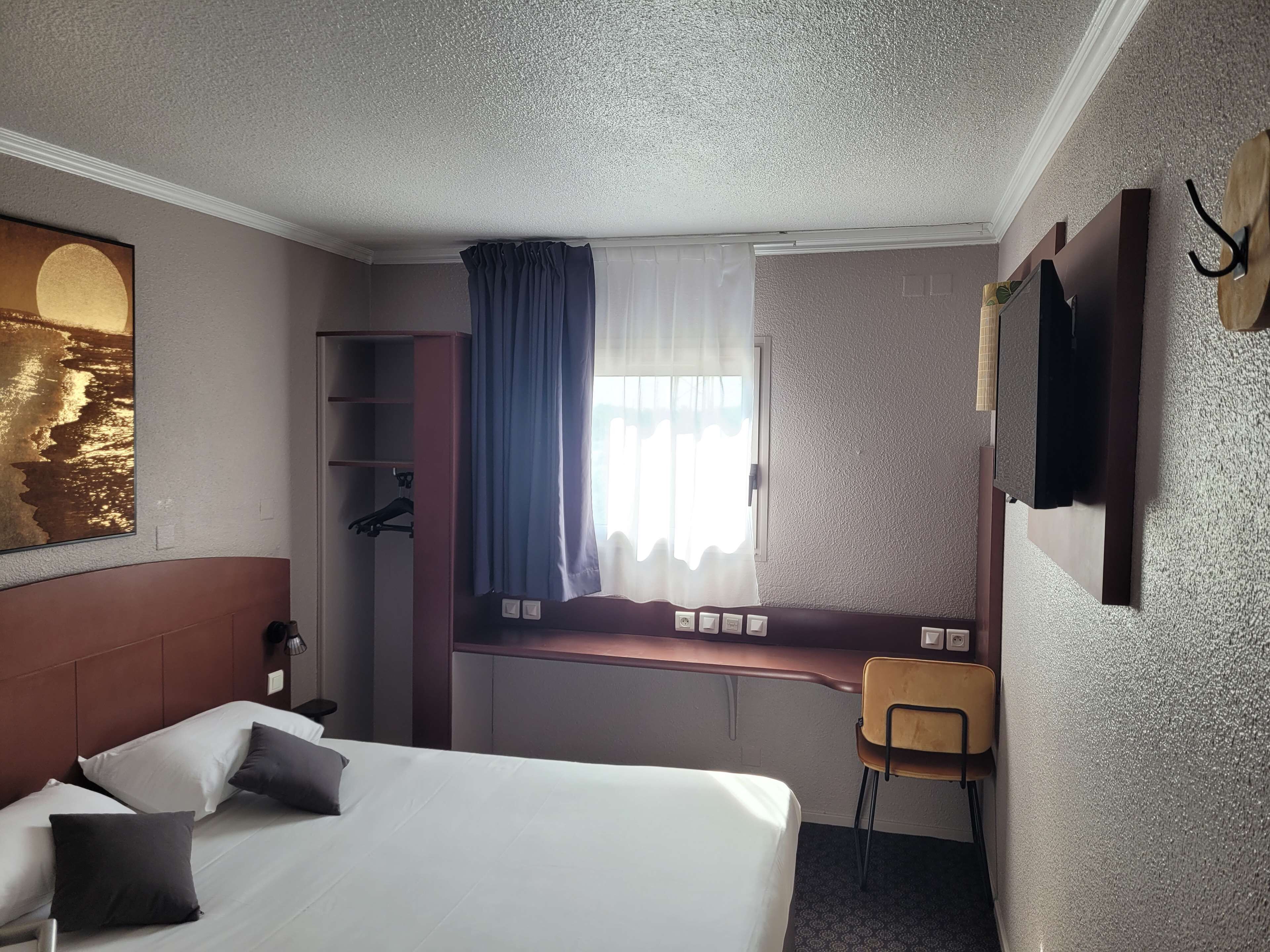 Una habitación de hotel con cama, escritorio, silla, armario y televisor.
