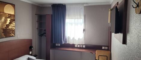 Una habitación de hotel con cama, escritorio, silla, armario y televisor.