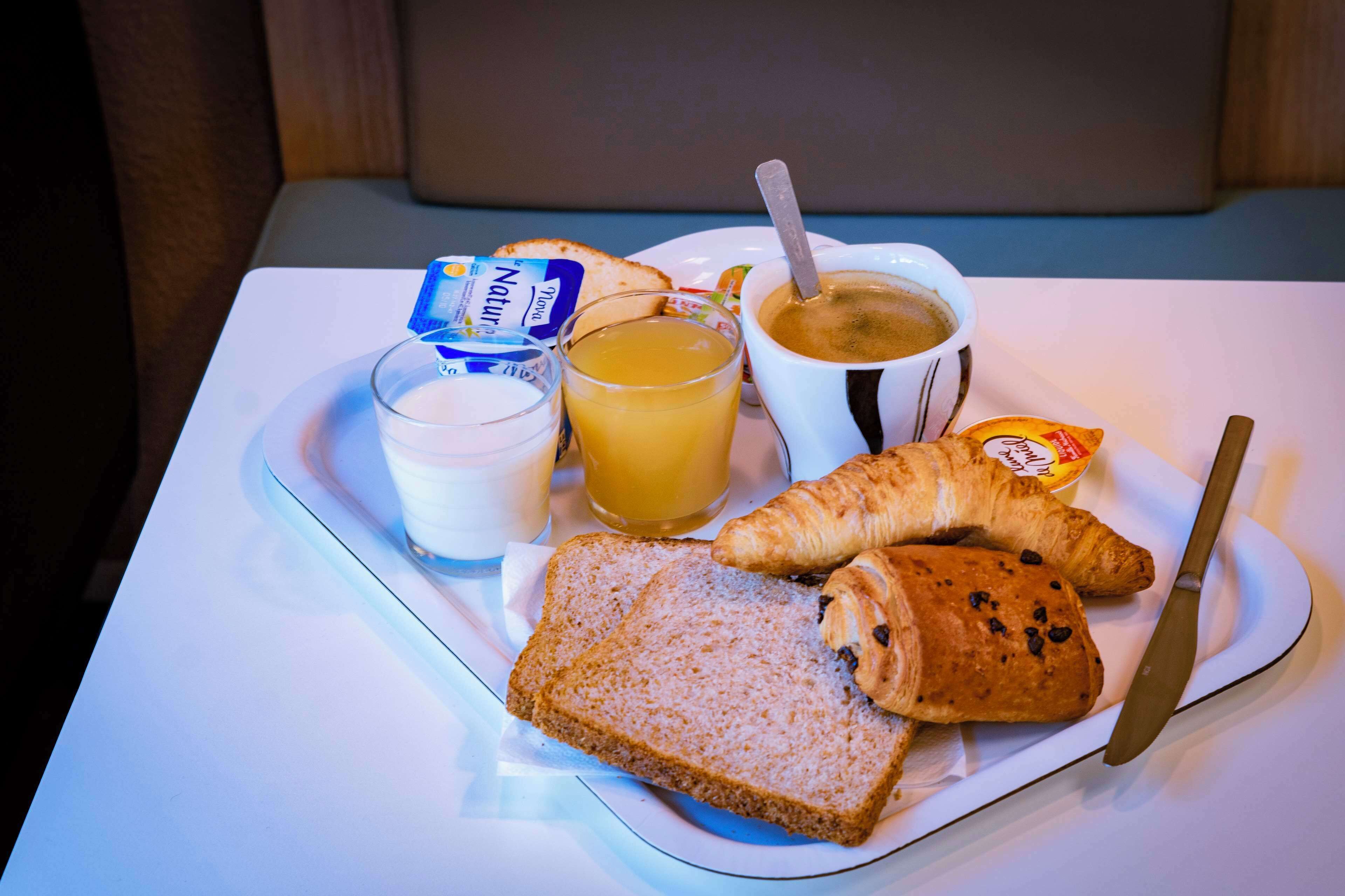A breakfast tray with toast, croissants, a cup of coffee, a glass of orange juice, and a packet of butter.
