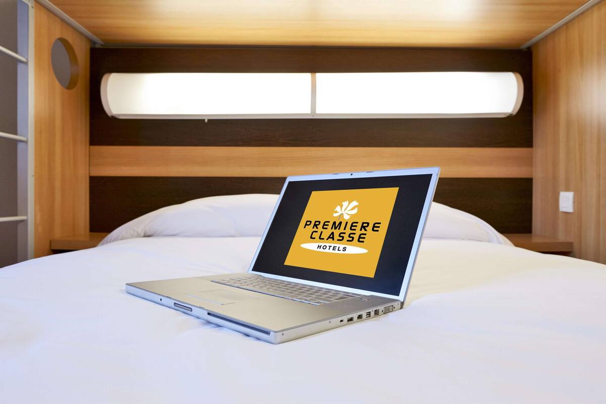 Una laptop sobre una cama con cabecera de madera y una ventana encima.