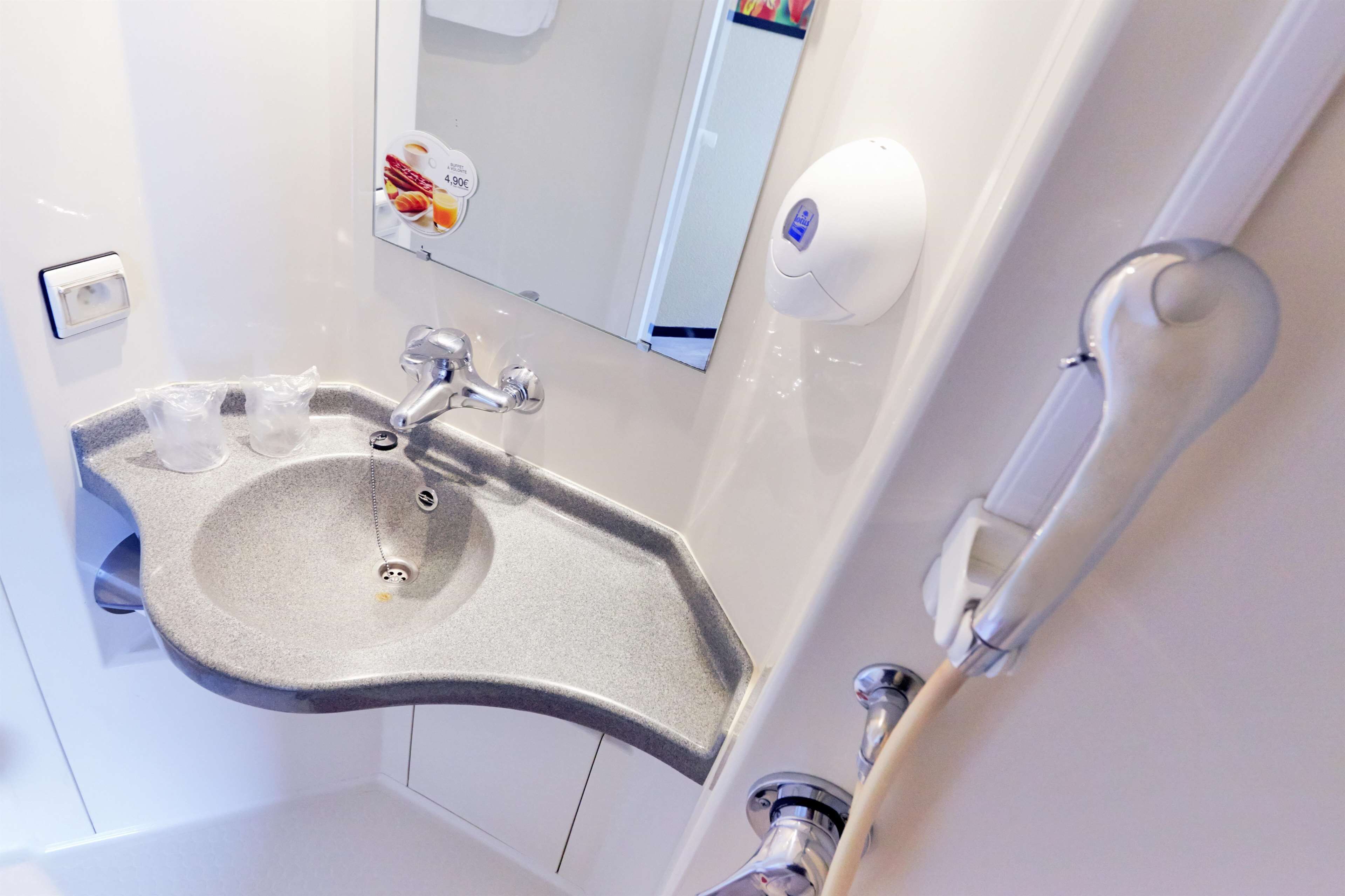 Un baño moderno con un lavamanos curvo, un espejo, un dispensador de jabón y un perchero para toallas.